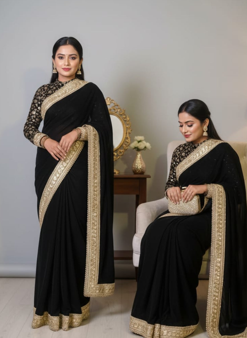 Two women in black sarees with gold borders in a room setting.